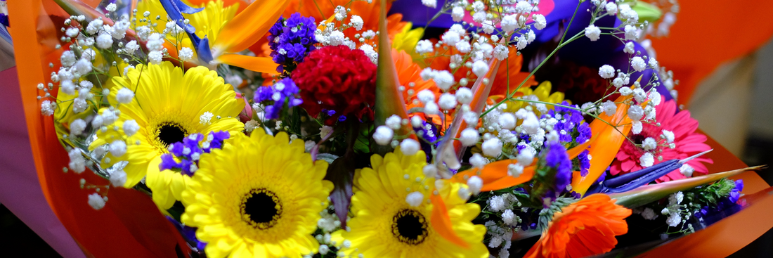 close up of bouquet of yellow gerberas, purple irises, orange roses and white baby's breath