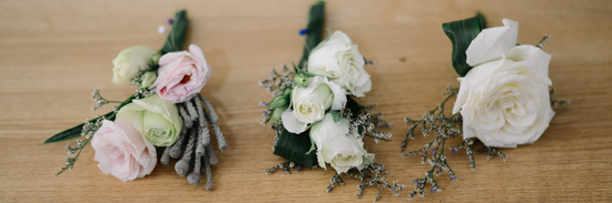 three beautiful corsages with corsage flowers featuring pink, light green and yellow spray roses on a wooden background
