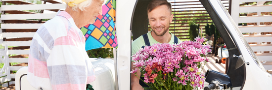 image of a delivery man in a van handing a beautiful bunch of purple carnations to an elderly lady for flower delivery Brisbane