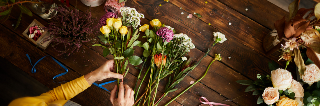 person in yellow shirt arranging flowers including yellow tulips and white roses on a brown wooden table