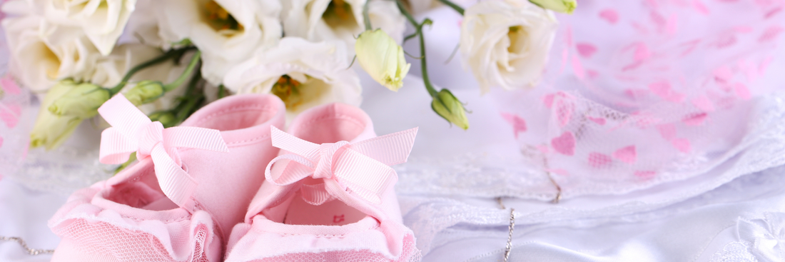 close up of pink baby shoes in front of white floral arrangement sitting atop pink fabric for flowers for baby girl