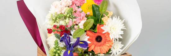 brightly coloured flower arrangement hand made by local florist with a red ribbon and white paper wrapped around it