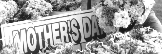 black and white photo of bunches of flowers wrapped in paper with a mother's day sign amongst them