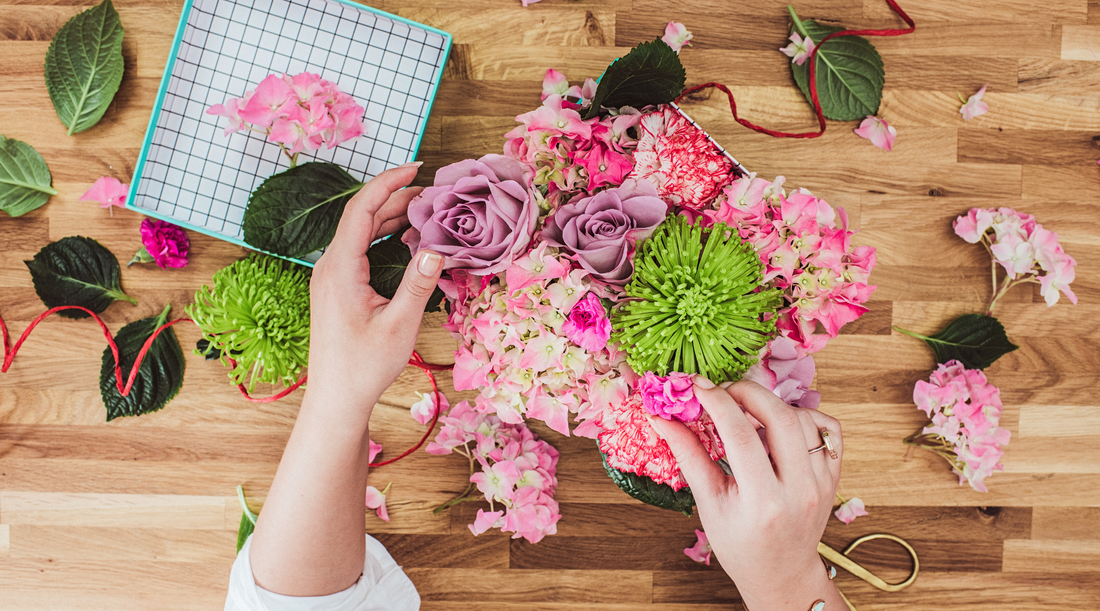 image of hands putting together a bouquet of fresh flowers with a polka dotted box to the left for gift wrapping with flowers